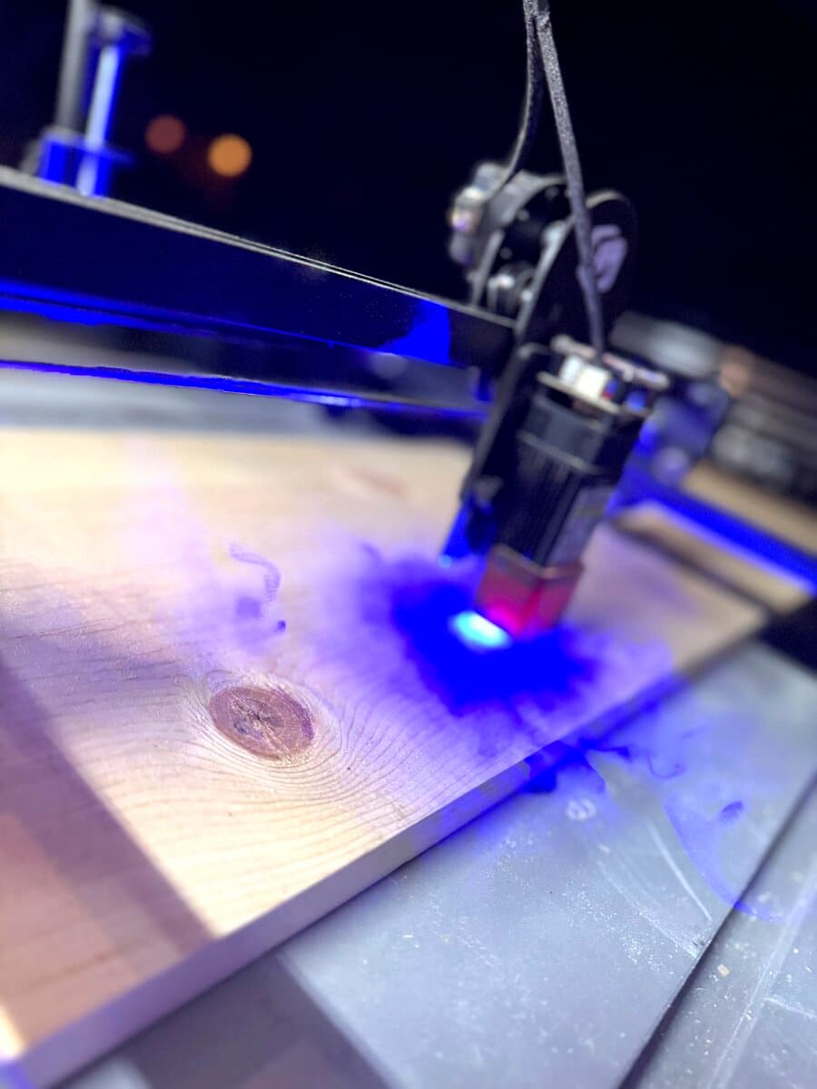 Laser engraver burning wood at night with blue glow and smoke